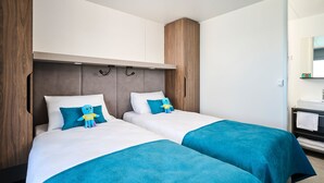 A hotel room with two beds, a wooden wardrobe, a small bathroom with a mirror and sink, and a blue plush toy on one of the beds. - Aminess Planet Camping Holiday Homes Sirena (Novigrad)