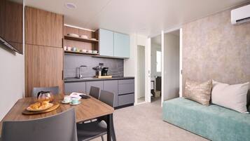 A modern kitchen with grey cabinets, a wooden dining table with chairs, and a teal sofa in the living area.