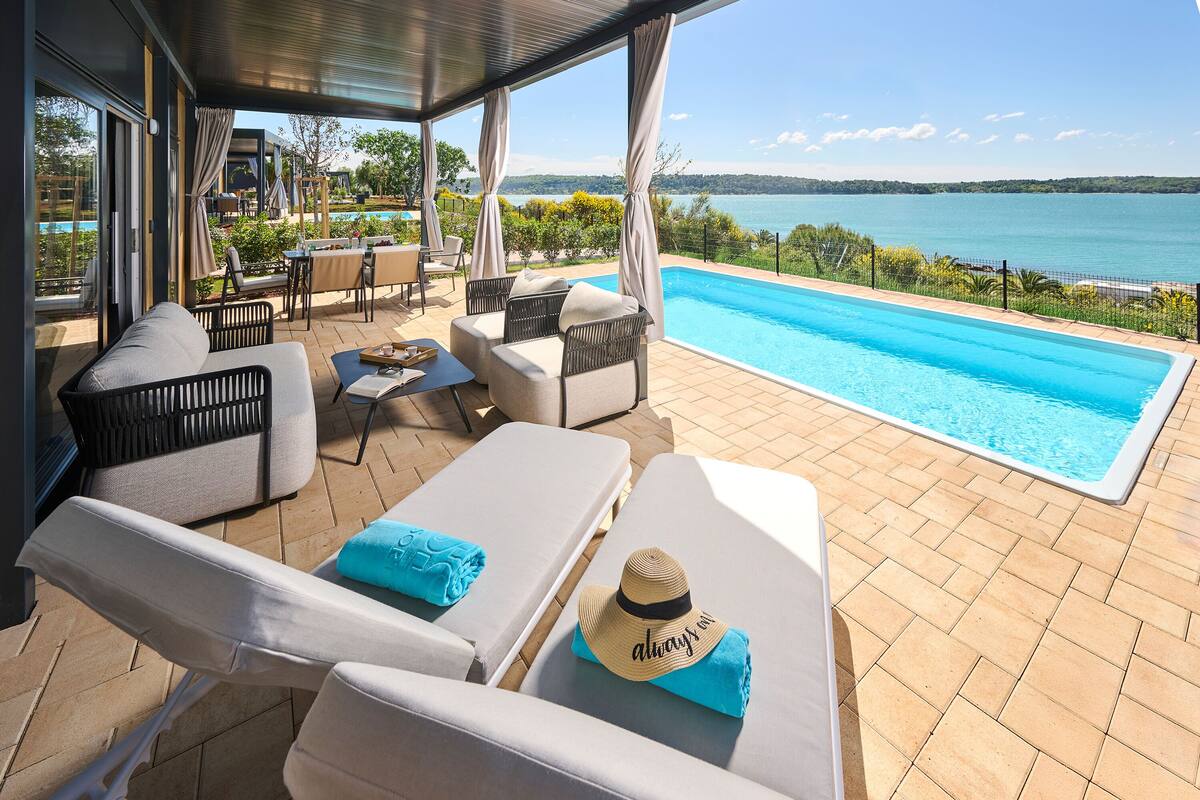 Un área junto a la piscina con sillones de descanso, una mesa y vistas al mar.