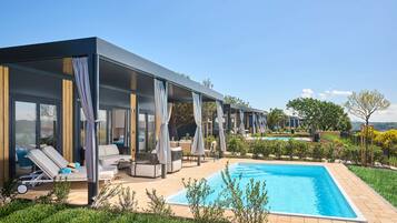 Un área de piscina moderna al aire libre con sillones de descanso y una zona de estar cubierta.