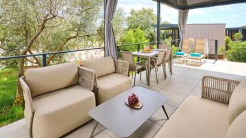 Un espacio al aire libre cubierto con sofás, una mesa y sillas, con vista a un jardín y un edificio.