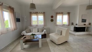 A spacious living room with a white sofa, a smaller armchair, a coffee table, and a fireplace. - Amazing Sea View Loft, Afitos (Afytos)