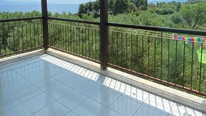 A covered balcony with a tiled floor, metal railing, and a view of a green landscape with trees and distant hills. - Amazing Sea View Loft, Afitos (Afytos)