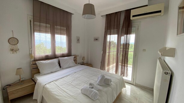 A bedroom with a bed, bedside tables, a lamp, a dreamcatcher, and a view of the outdoors. - Amazing Sea View Loft, Afitos (Afytos)