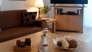 Een woonkamer met een bank, een salontafel met decoratieve objecten, een televisie op een meubel en ingelijste foto's aan de muur.