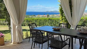 Een terras buiten met een tafel en stoelen, met uitzicht op een prachtig zee- en heuvellandschap.