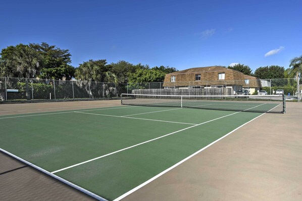 Un court de tennis avec un filet, entouré d’une clôture et d’arbres.