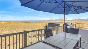 Eine Terrasse mit Tisch, Stühlen, einem Grill und Blick auf einen See und Berge.