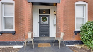 A brick building with a black door, a wreath, and two metal chairs on the steps.
