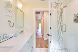 A bathroom with a white vanity, a large mirror, and a shower with a geometric tile pattern. - Walk to Ocean: Home w/ Pool in Holmes Beach (Holmes Beach)