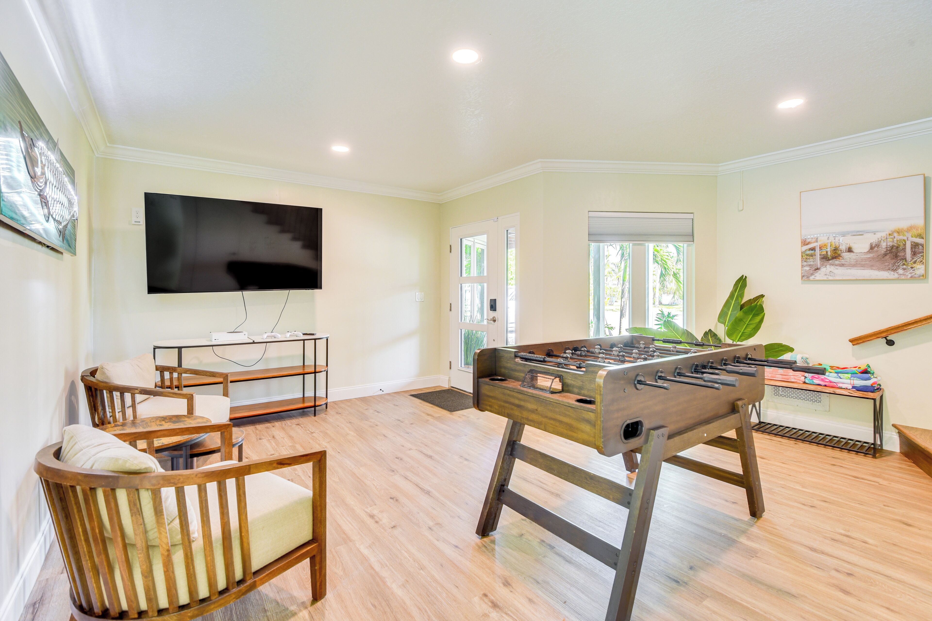 A living room with a foosball table, a flat-screen TV, wooden furniture, and a large window with a view.