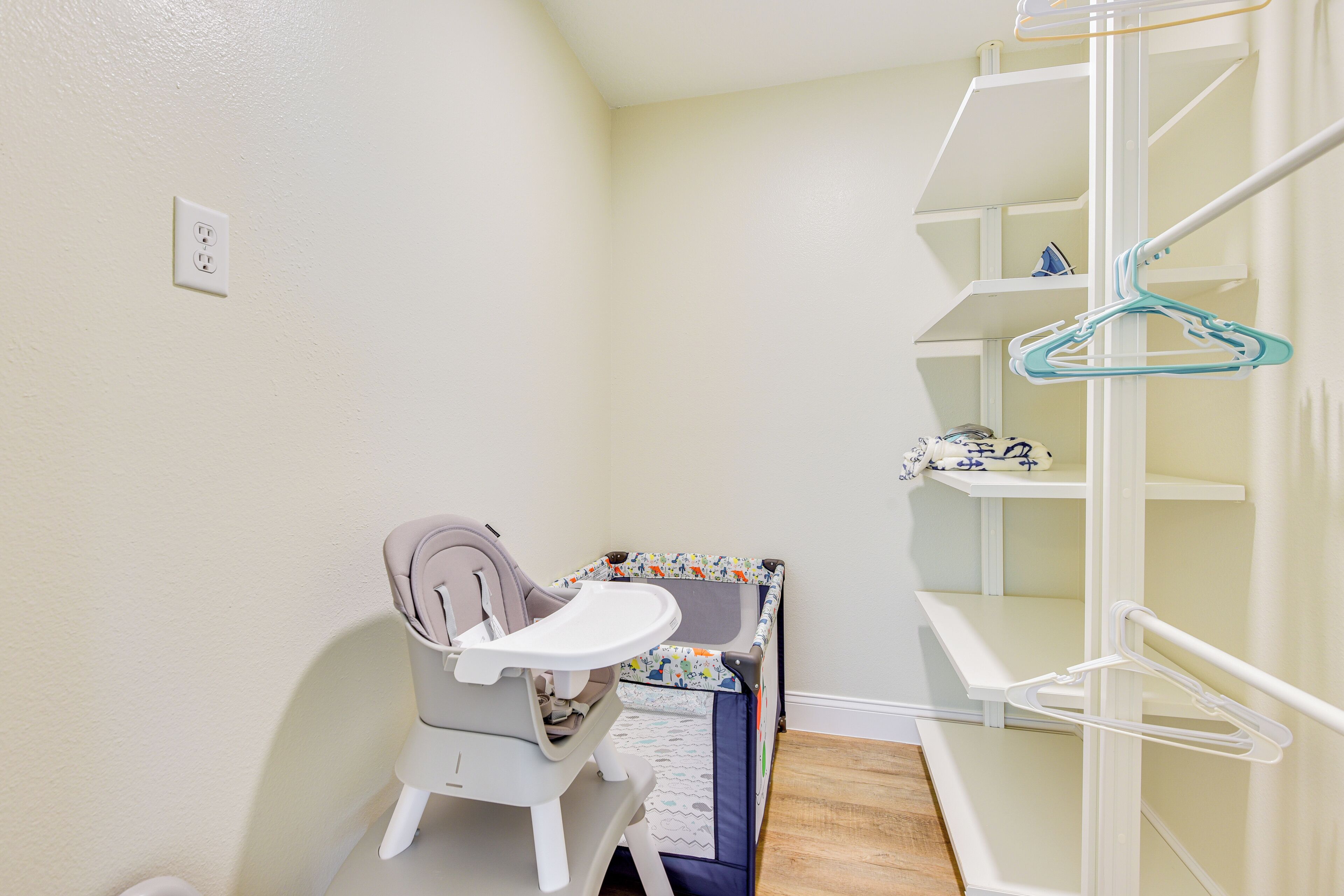 Ein Zimmer mit weißer Wand, einem weißen Stuhl mit Tablett, einem kleinen Tisch und einem weißen Regal mit Kleiderhaken.