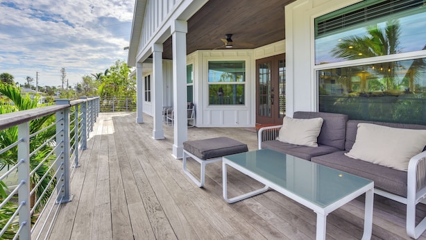 A covered outdoor area with a wooden deck, a glass table, and a sofa with cushions. - Walk to Ocean: Home w/ Pool in Holmes Beach (Holmes Beach)