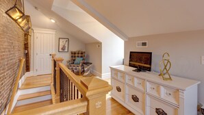 A staircase with wooden steps and a railing, leading to a room with a white dresser, a television, and a framed picture on the wall. - Walkable Area: Spacious Apt in Dtwn St Louis (St. Louis)