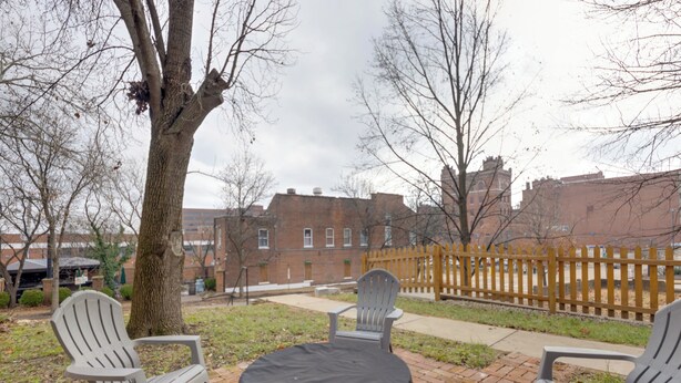 A patio area with two Adirondack chairs and a round table, surrounded by a brick wall and a wooden fence. - Walk to Anheuser-busch Brewery: St Louis Escape! (St. Louis)