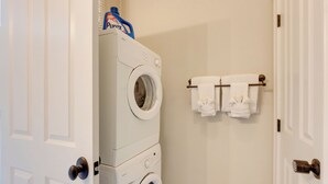 A laundry area with a front-loading washer and dryer, a wall-mounted towel rack with several towels, and a door with a doorknob. - Walk to Anheuser-busch Brewery: St Louis Escape! (St. Louis)