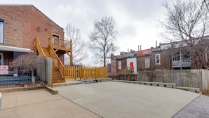 A concrete patio area with a wooden staircase leading to a balcony, surrounded by brick buildings and a wooden fence. - Walk to Anheuser-busch Brewery: St Louis Escape! (St. Louis)