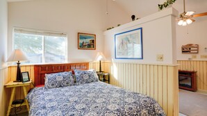 Une chambre à coucher avec un grand lit, une tête de lit en bois, deux tables de chevet avec des lampes, une fenêtre avec des stores et un ventilateur de plafond.