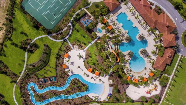 Luchtbeeld van een resort met een groot zwembad, een tennisbaan en een kronkelend waterpartij.