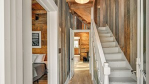 Un interior de madera con una escalera, una cama y un cuadro en la pared.