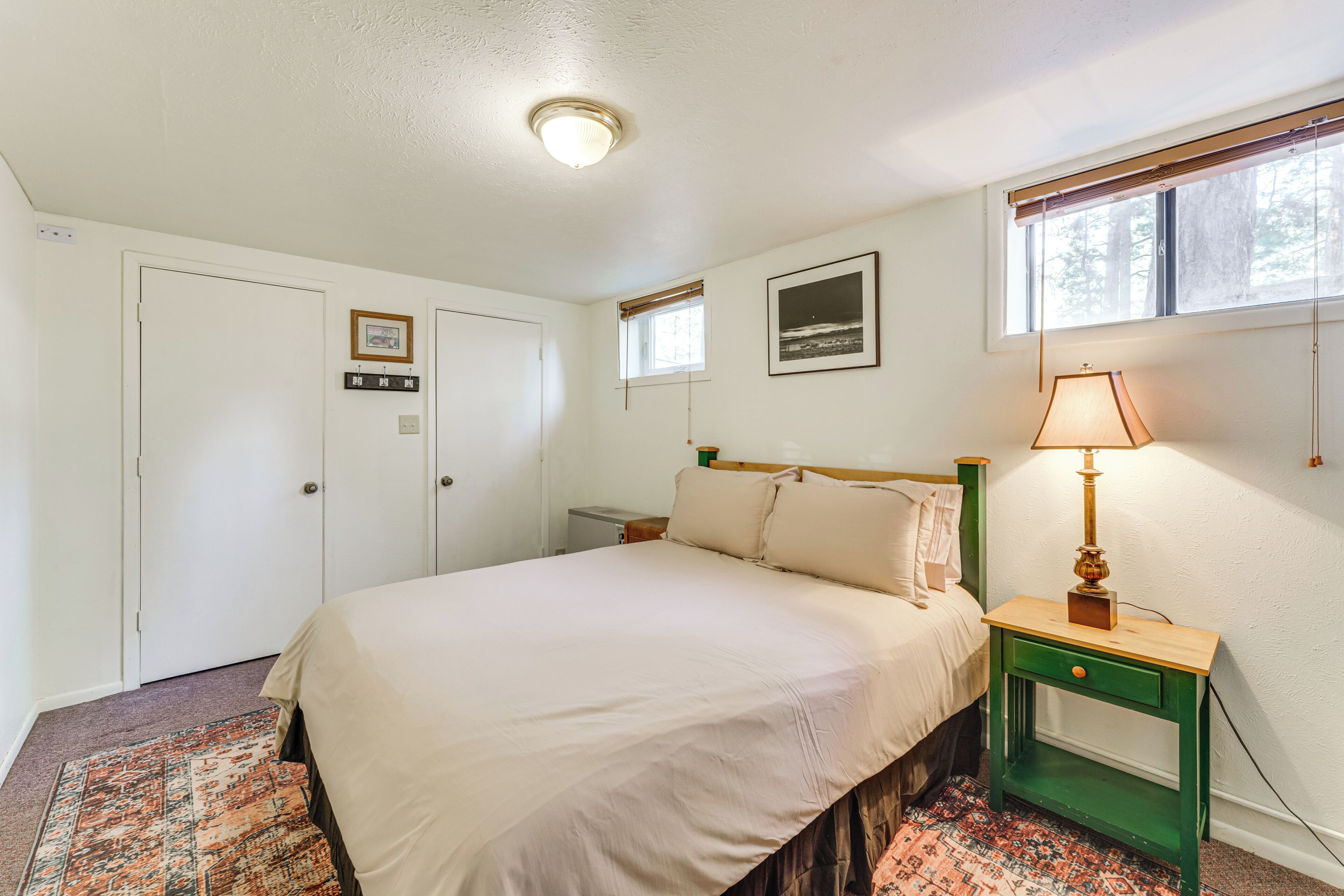 Quarto com cama, mesa de cabeceira, abajur, janela e porta.