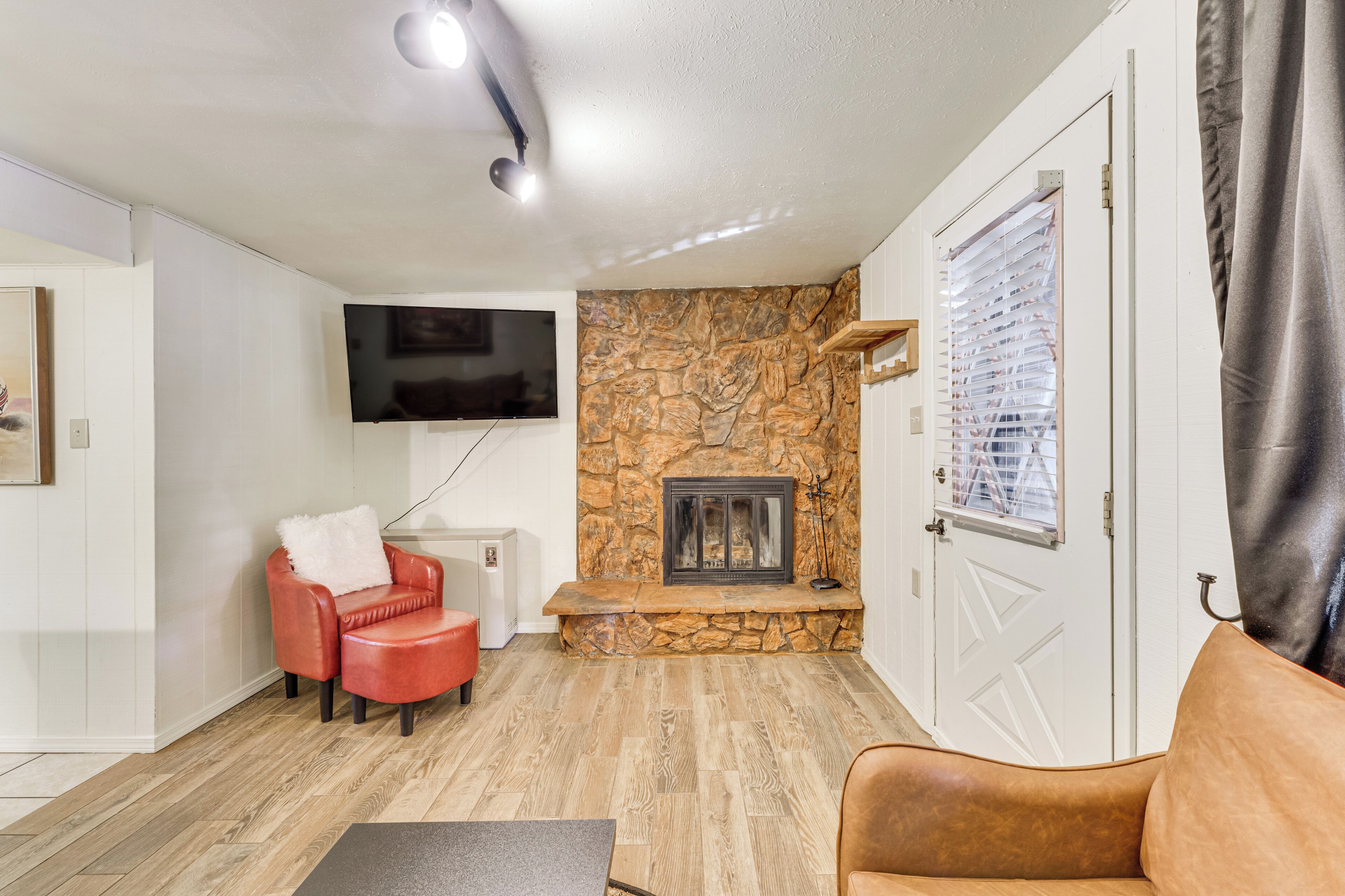 A living room with a stone fireplace, a television mounted on the wall, and a red leather chair.