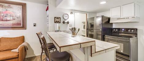 Una cocina moderna con una isla central, electrodomésticos de acero inoxidable y un comedor con sofá y sillas.