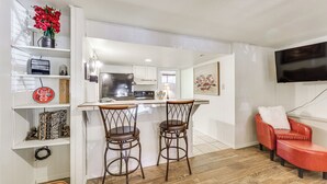 A modern kitchen with white cabinets, a central island with two bar stools, a red leather chair, and a flat-screen TV mounted on the wall. - Walk to Angel Fire Resort: Condo w/ Furnished Deck (Angel Fire)