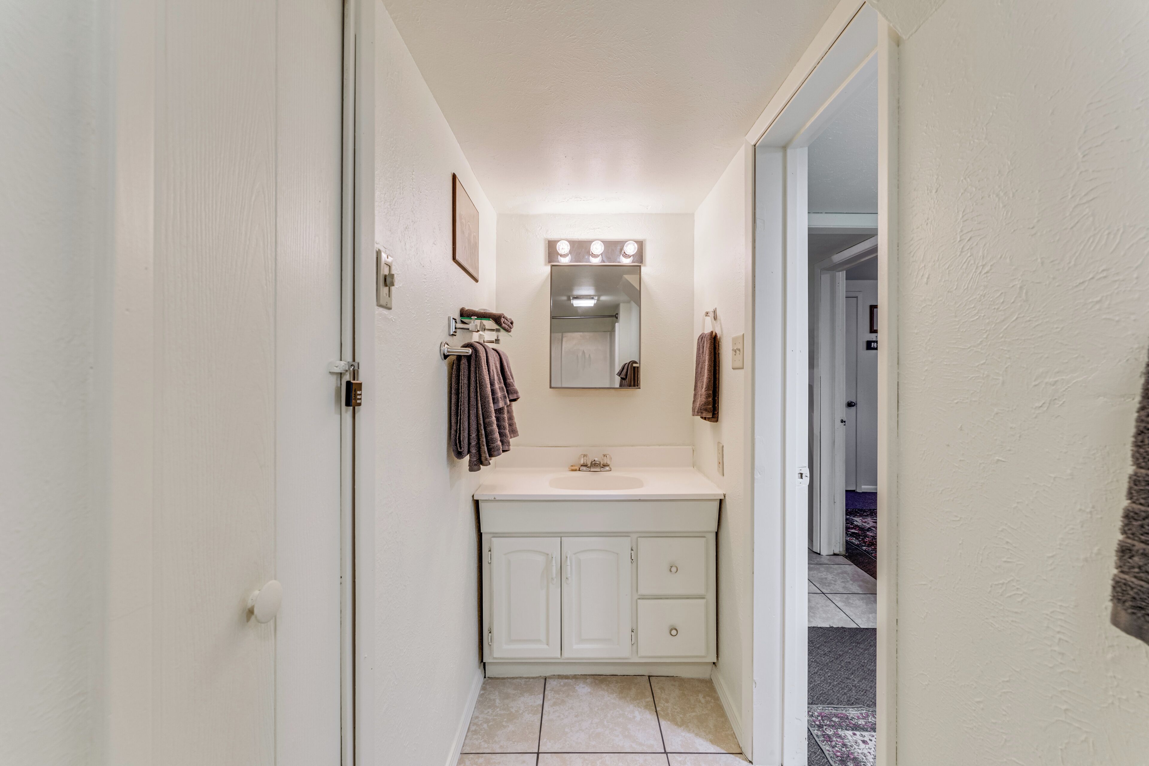 A narrow bathroom with a white sink, mirror, and towel rack.