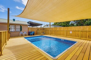 Ett trädäck med en swimmingpool, omgivet av ett trästaket och ett område med skugga.