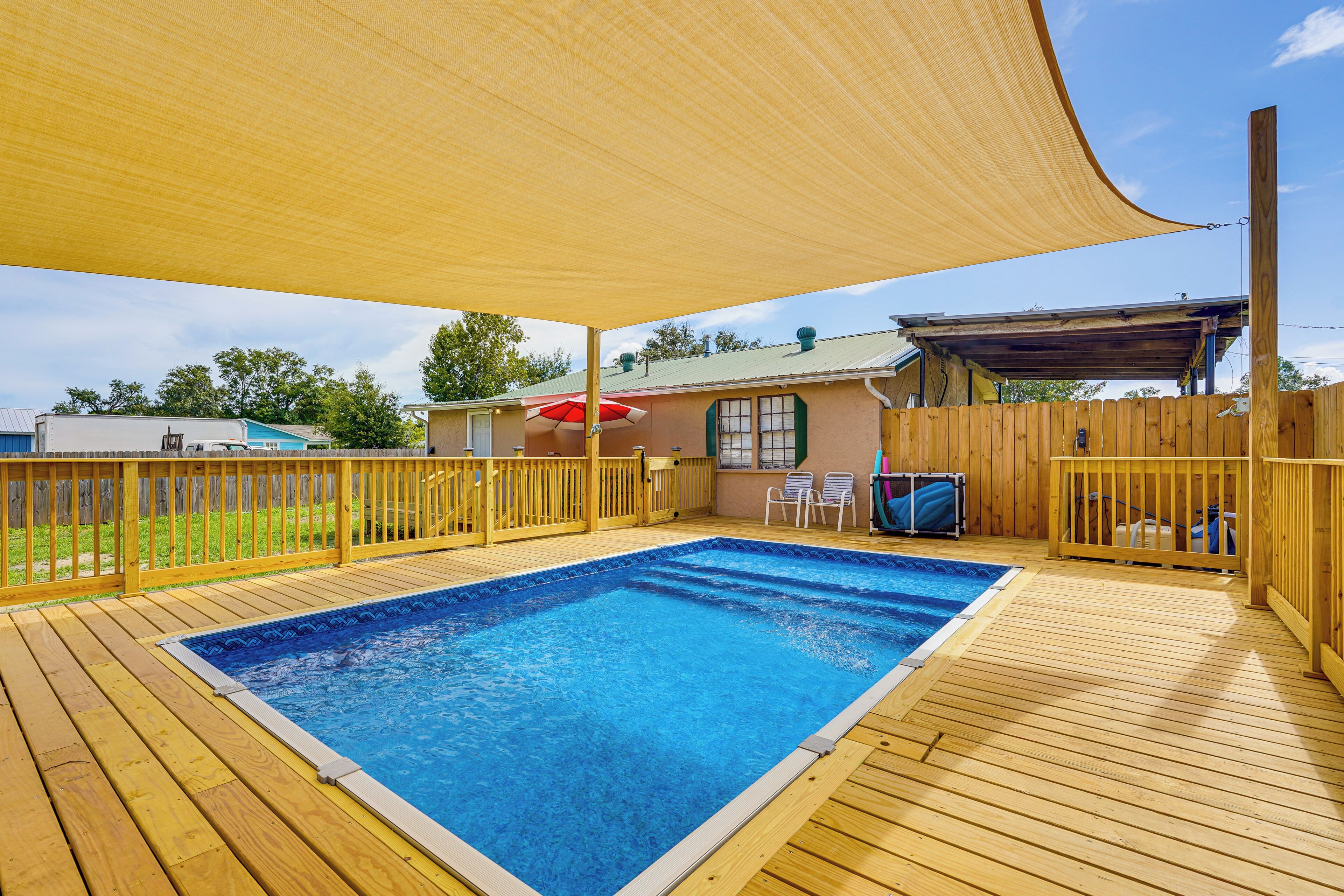 A wooden deck with a swimming pool, a covered area with a red umbrella, and a wooden fence.