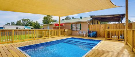 A wooden deck with a swimming pool, a covered area with a red umbrella, and a wooden fence.