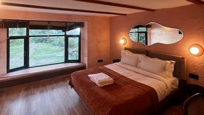 Een slaapkamer met een groot bed, houten balken, een raam met uitzicht en een spiegel aan de muur.