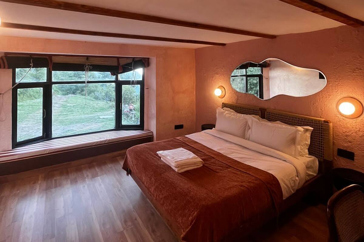 A bedroom with a large bed, wooden beams, a window with a view, and a mirror on the wall.
