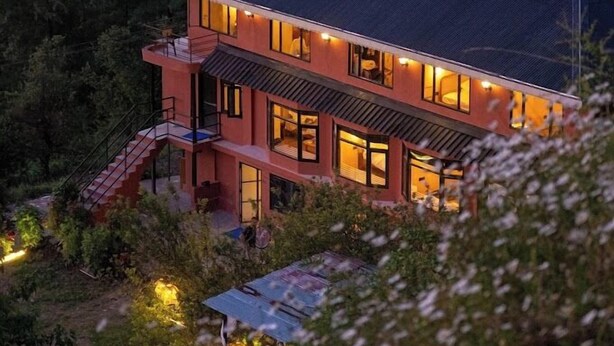 Een huis met twee verdiepingen en een plat dak, omgeven door dicht bos.