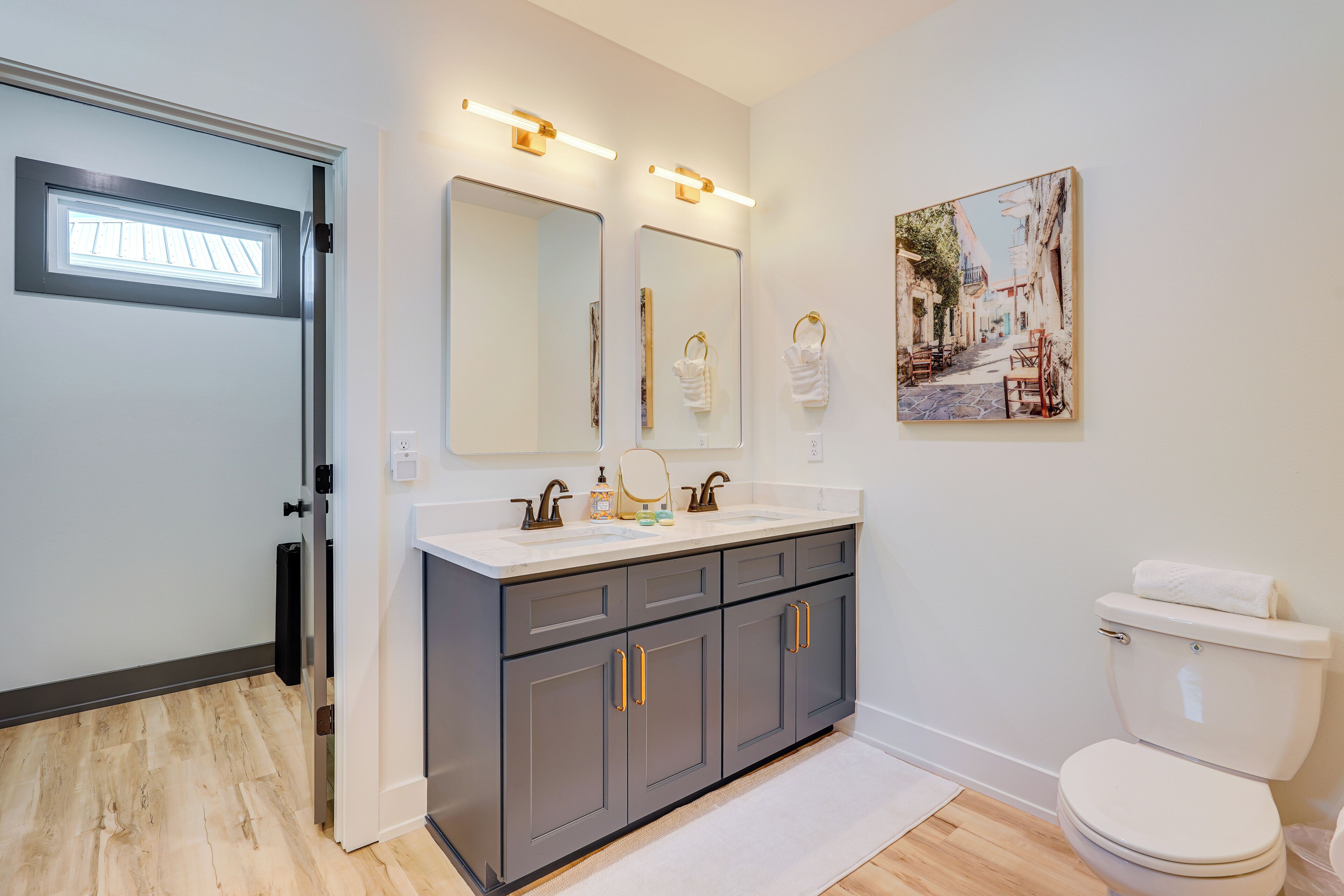 A modern bathroom with a double vanity, a toilet, and a large mirror.