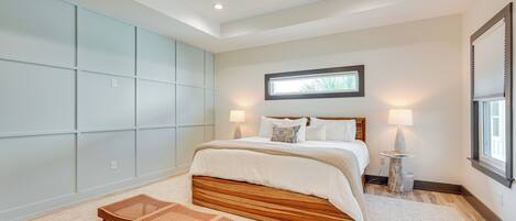 A bedroom with a large bed, a ceiling fan, a window with blinds, and a bedside table with a lamp.