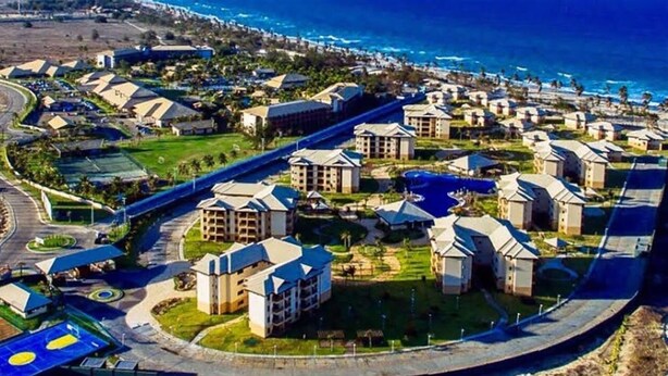 An aerial view of a resort with multiple buildings, a central road, and a coastline in the background. - Ground floor apartment, in the VG Sun condominium. Condominium right on the sand. (Caucaia)