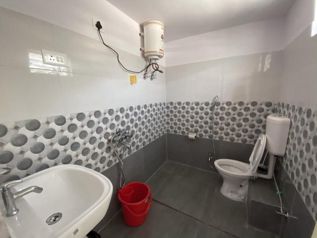 A bathroom with a white sink, toilet, and shower. There is a red bucket on the floor.