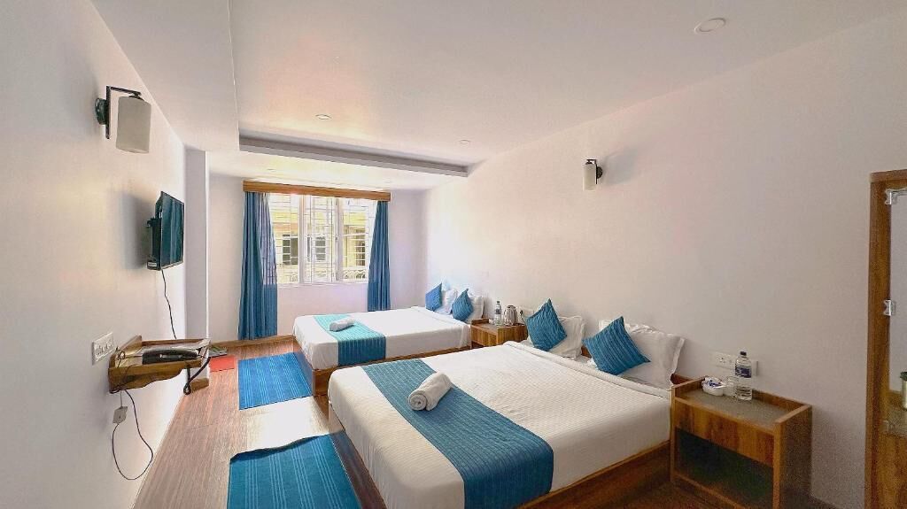Une chambre d’hôtel avec deux lits, une télévision, une fenêtre avec des rideaux et un plancher en bois.