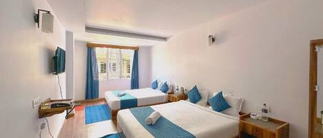 Habitación de hotel con dos camas, televisión, ventana con cortinas y suelo de madera.