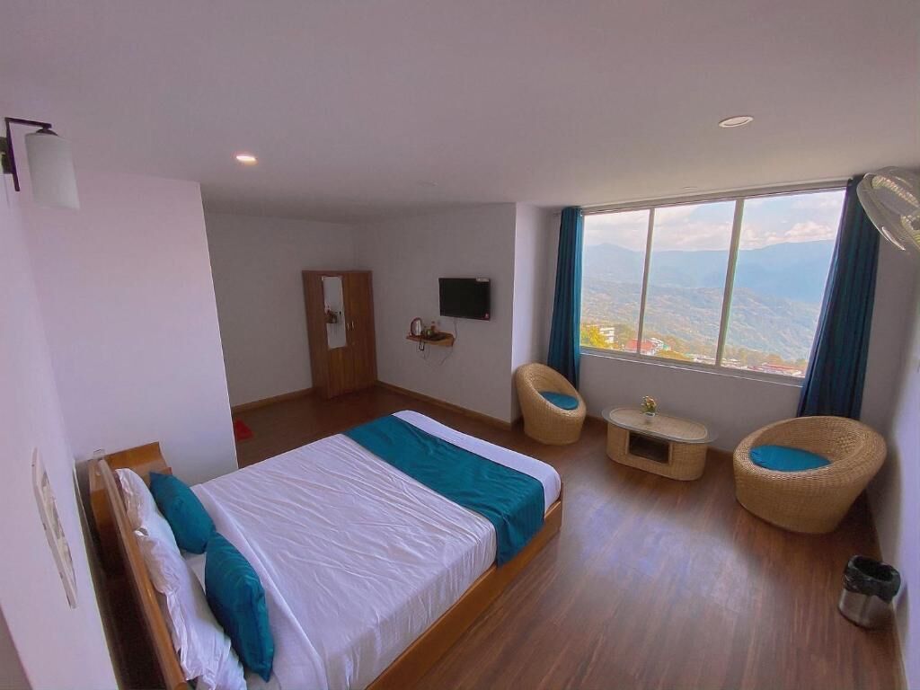 Een hotelkamer met een groot bed, twee rieten stoelen, een tafeltje, een televisie en uitzicht op de bergen.