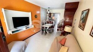 A living room with a TV, orange walls, a dining area, and a kitchen.