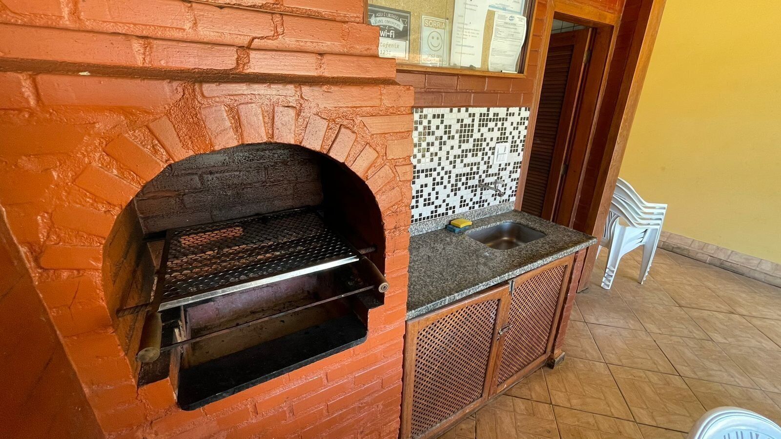A brick oven with a metal rack, a tiled backsplash, and a sink above it.