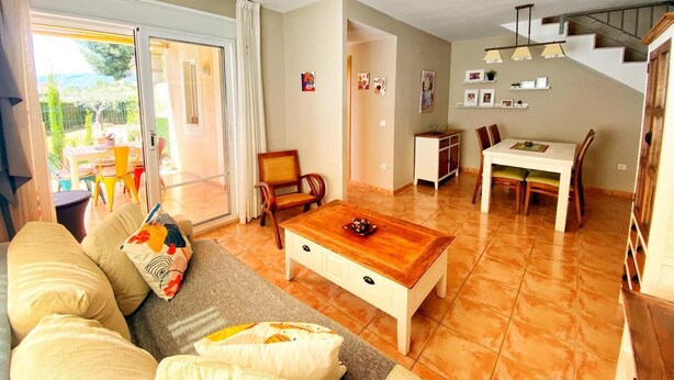 A spacious living room with a sofa, coffee table, and dining area. There is a staircase leading to an upper level. - House with private garden, BBQ community pool and WiFi (Mont-roig del Camp)