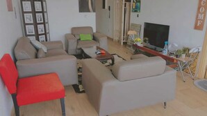 A living room with a sofa set, a red chair, a TV, and a small table with items on it. - Furnished studio in DAKAR quiet in a building with security and comfort assured (Dakar)