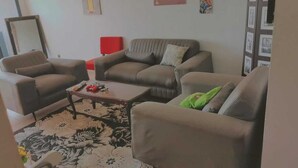 A living room with a brown sofa set, a coffee table, and a red chair. - Furnished studio in DAKAR quiet in a building with security and comfort assured (Dakar)