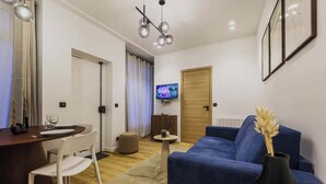 Ein modernes Wohnzimmer mit einem blauen Sofa, einem Esstisch mit Stühlen, einem an der Wand montierten Fernseher und einer Holztür.