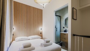 Ein Hotelzimmer mit Bett, einer Wand aus Holzlatten, einem Badezimmer mit Spiegel und einer Treppe.