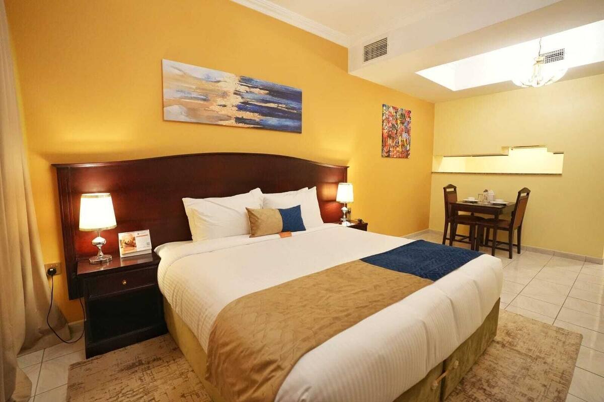 A hotel room with a large bed, two bedside tables with lamps, a desk with a chair, and artwork on the walls.